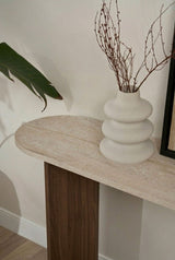 Moderna mesa auxiliar ovalada con tapa de aspecto travertino y base de melamina de nogal. Diseño minimalista y elegante.